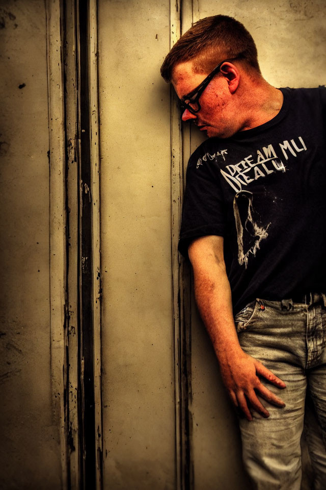 Man in glasses leans against textured wall in contemplative pose