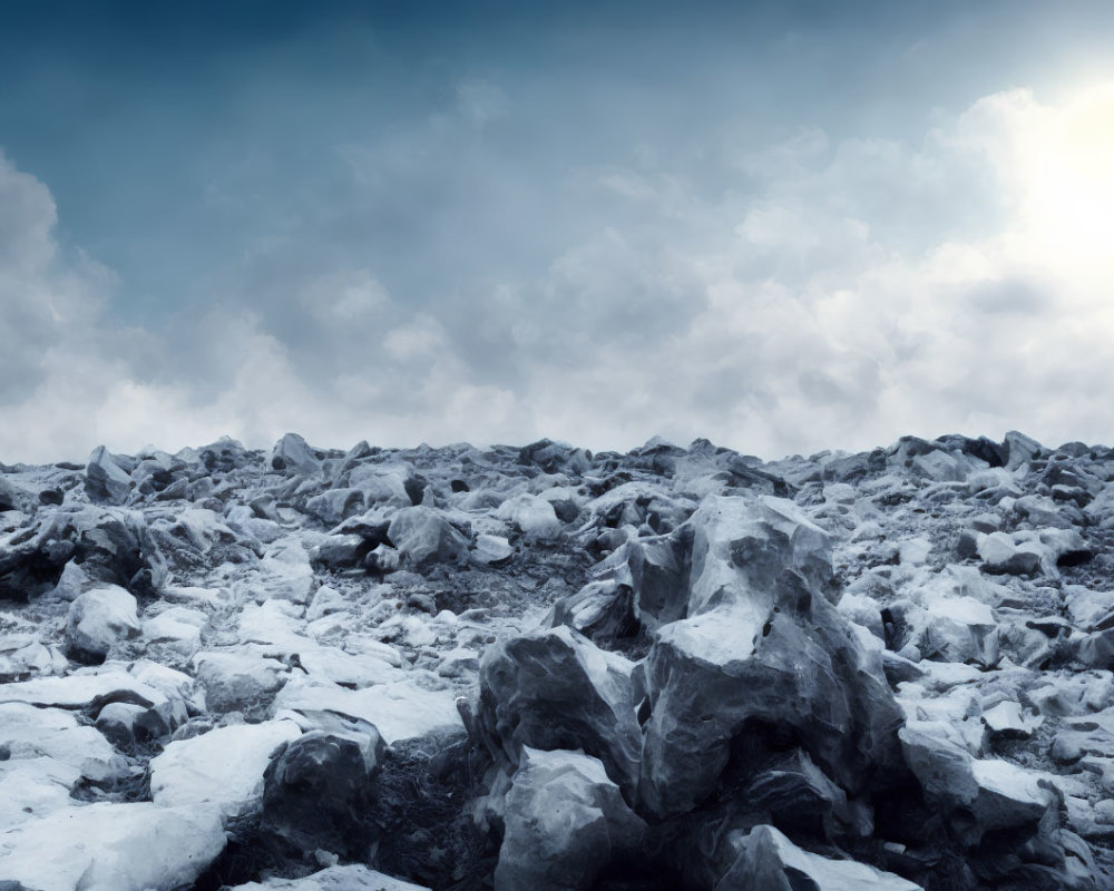 Snow-covered rocky terrain under cloudy sky with sun peeking through