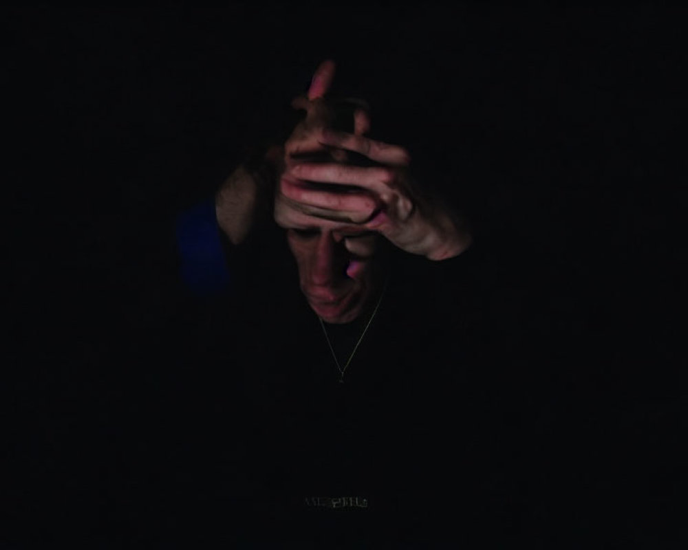 Person with clasped hands in dim lighting, showing contemplation.