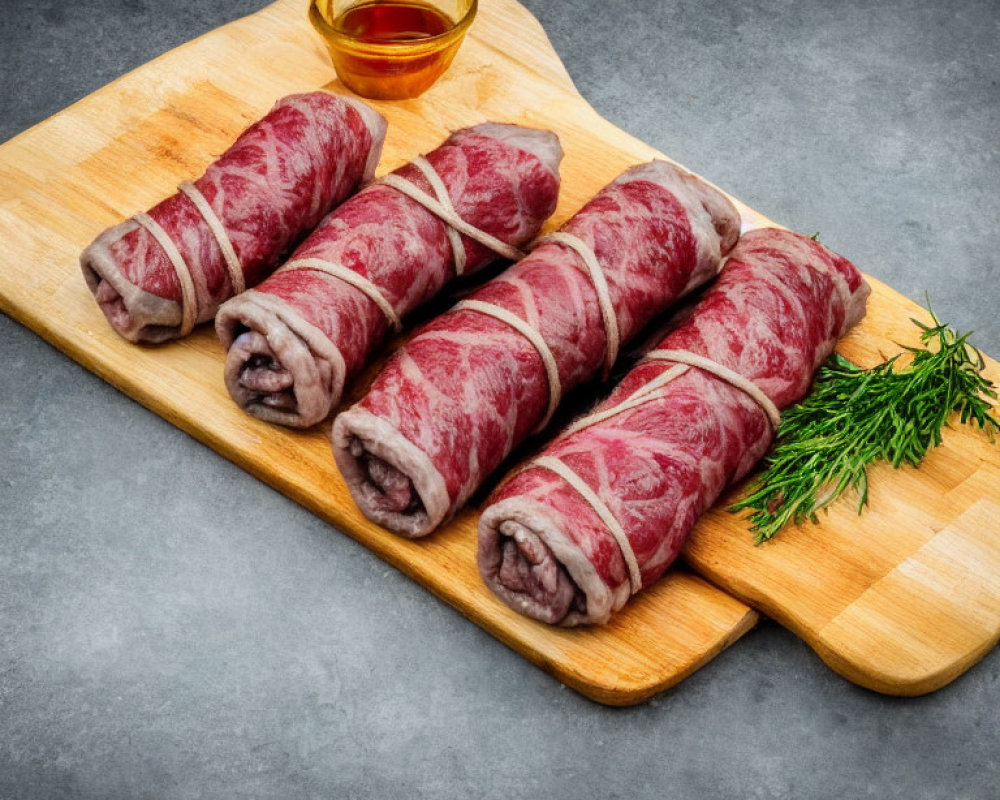 Raw beef rolls with string on wooden board with dill and sauce