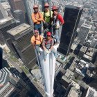 Three people posing on skyscraper ledge with city skyline view