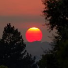 Eerie mountain landscape under a blood-red sun with glowing red eyes