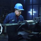 Blue hard hat worker operates industrial lathe in dimly lit workshop