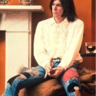 Seated person with dark hair, cream shirt, blue jeans, fridge, and bird.