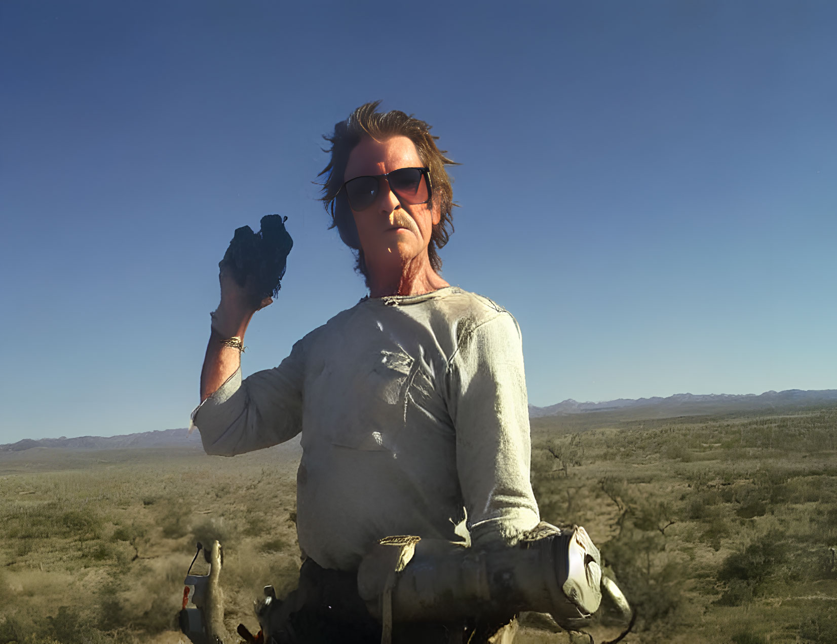 Person in Desert Landscape Wearing Sunglasses Holding Black Object