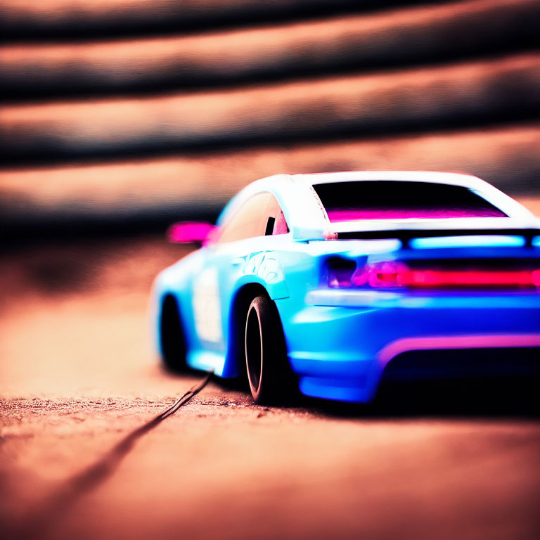 Miniature blue toy car with pink underglow on textured surface in motion.