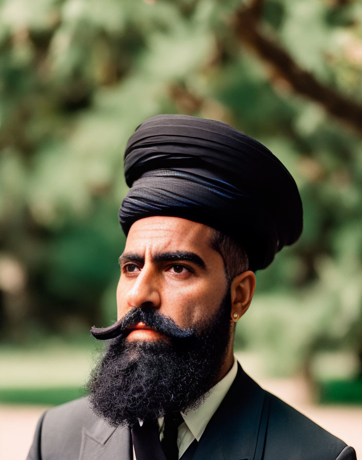 Styled bearded man in turban against green foliage background