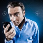 Man in Blue Shirt Holding Smartphone in Soft Lighting