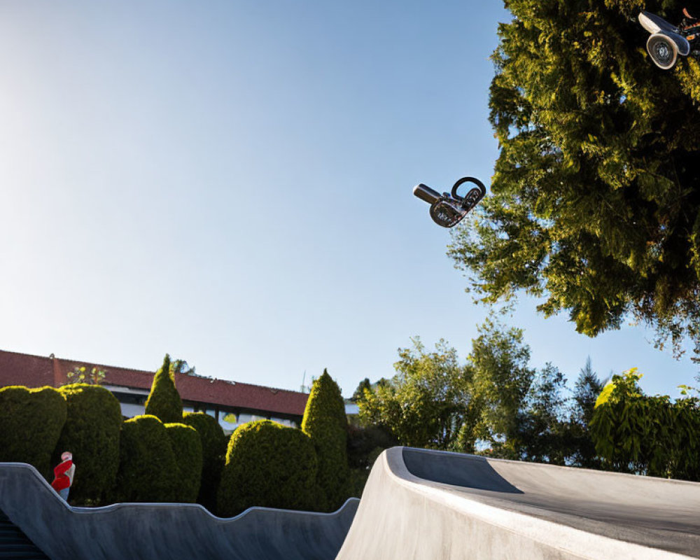 BMX rider mid-air trick over skatepark ramp with blue sky & green foliage