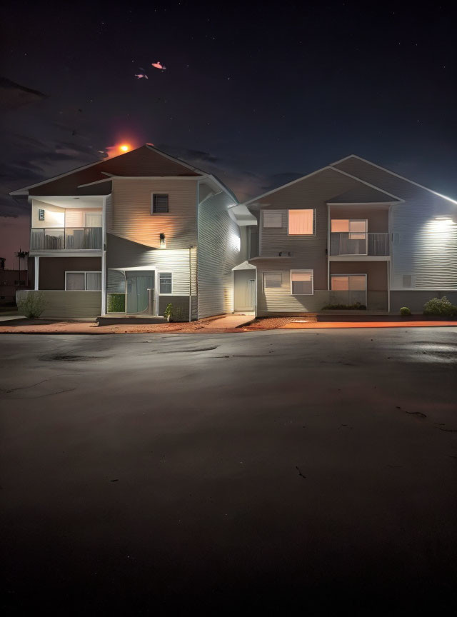 Night scene of two-story residential buildings with lit windows under starry sky