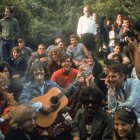 Psychedelic band in 60s-inspired outfits with sunglasses, surrounded by colorful aura in forest setting