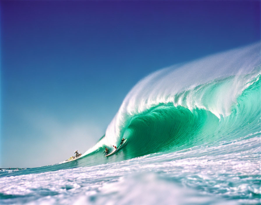 Surfer riding towering turquoise wave with jet ski in background