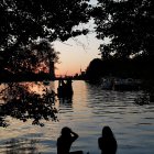 Silhouetted Figures by River at Sunset with Boats and Tower