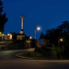 Stylized nocturnal landscape with rolling hills, illuminated houses, spire, trees, crescent