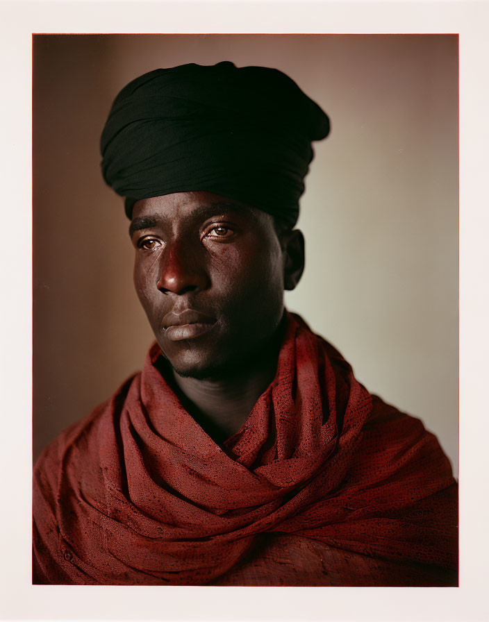 Dark-skinned man in black turban and red scarf gazing right thoughtfully