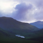 Tranquil landscape: rolling hills, calm lake, boulders, fluffy clouds at dusk or