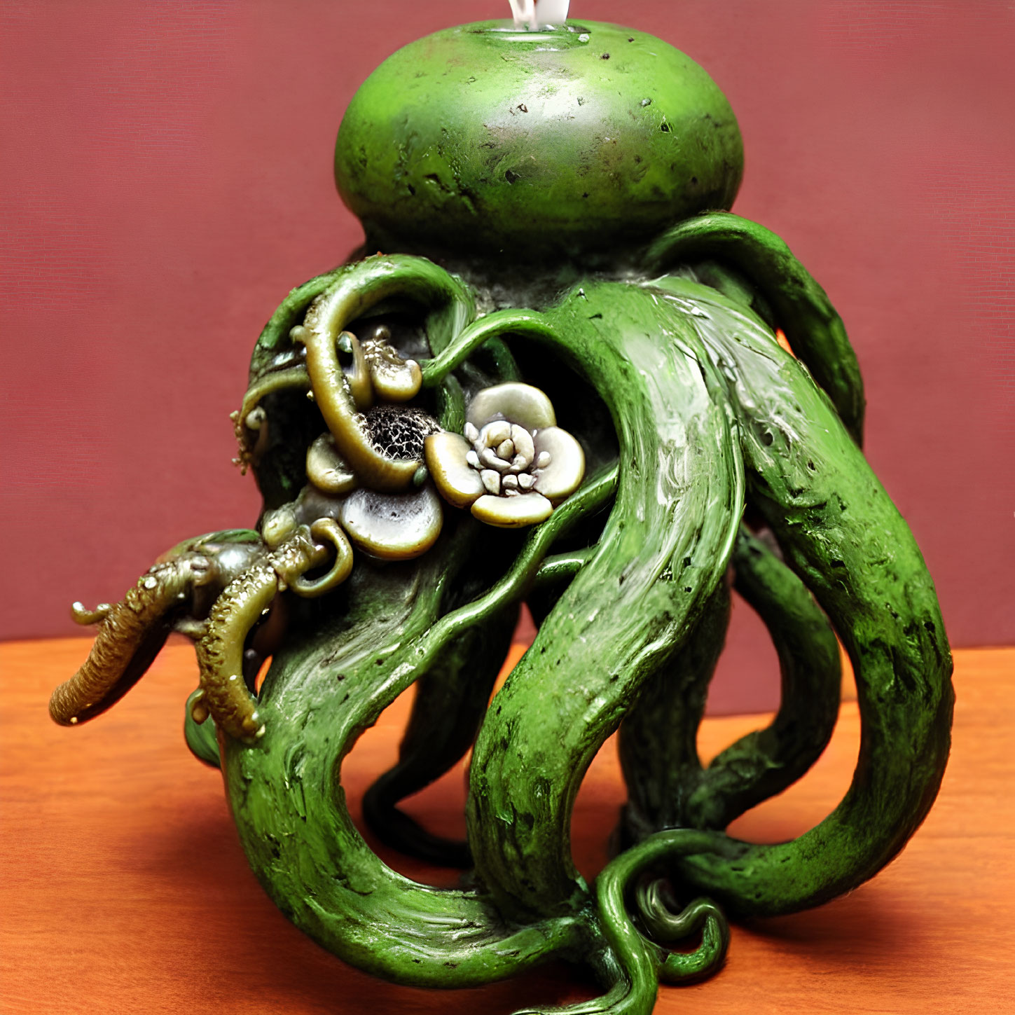 Intricately designed green candle with tentacle-like shapes and floral elements on pink background