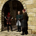 Three people in historical attire by arched stone doorway