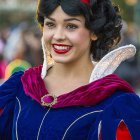 Woman in Snow White costume with red headband and dark hair smiling in front of bokeh background