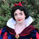 Person in Snow White costume with blue and red gown against leafy backdrop