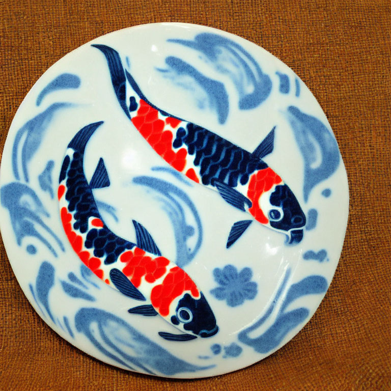 Circular ceramic plate with orange and black koi fish on blue and white wave design