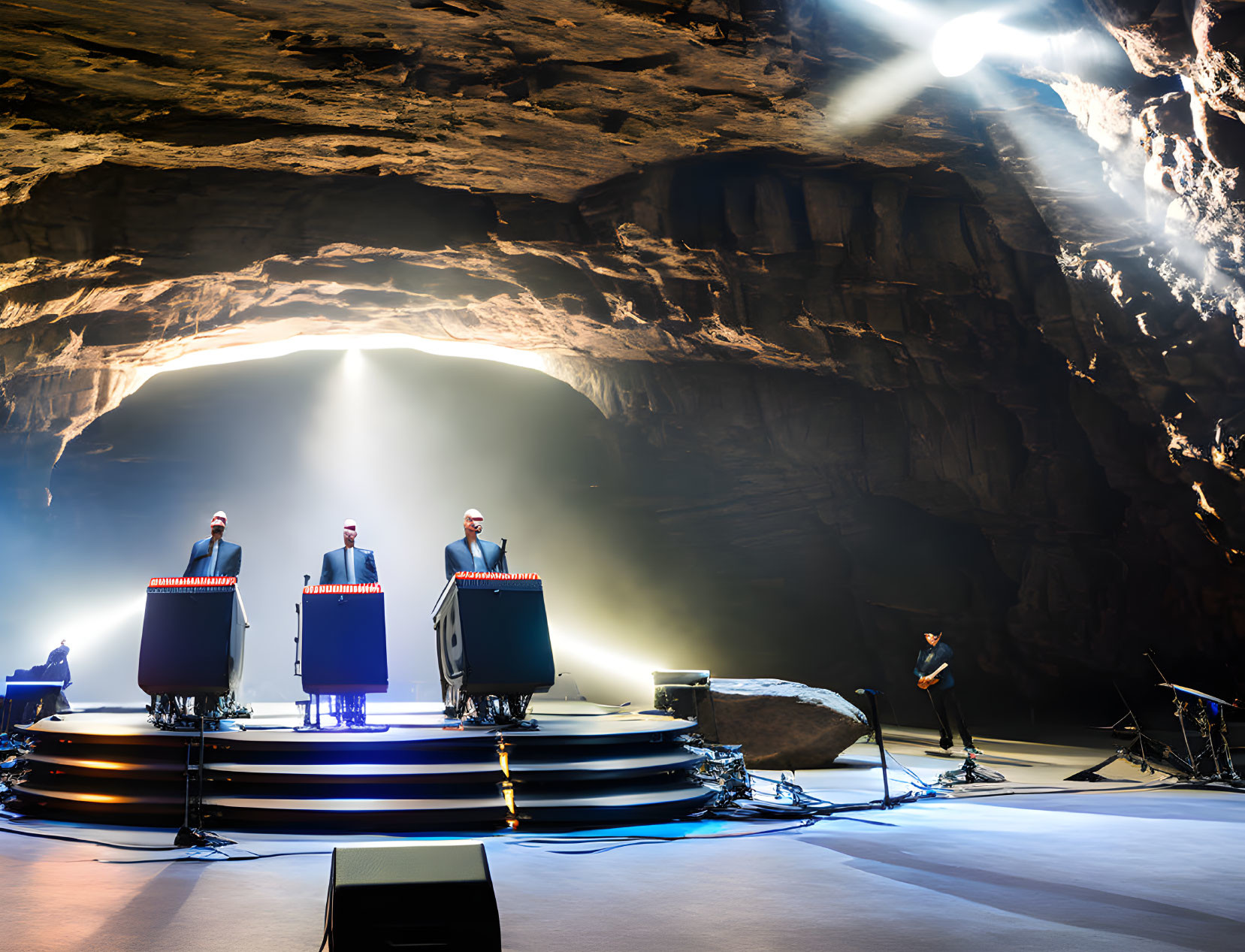 Band performing in cavernous space with light beams.