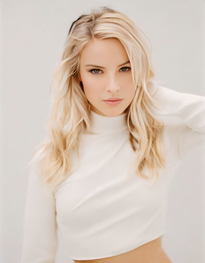 Blonde woman with wavy hair in white top posing with subtle gaze
