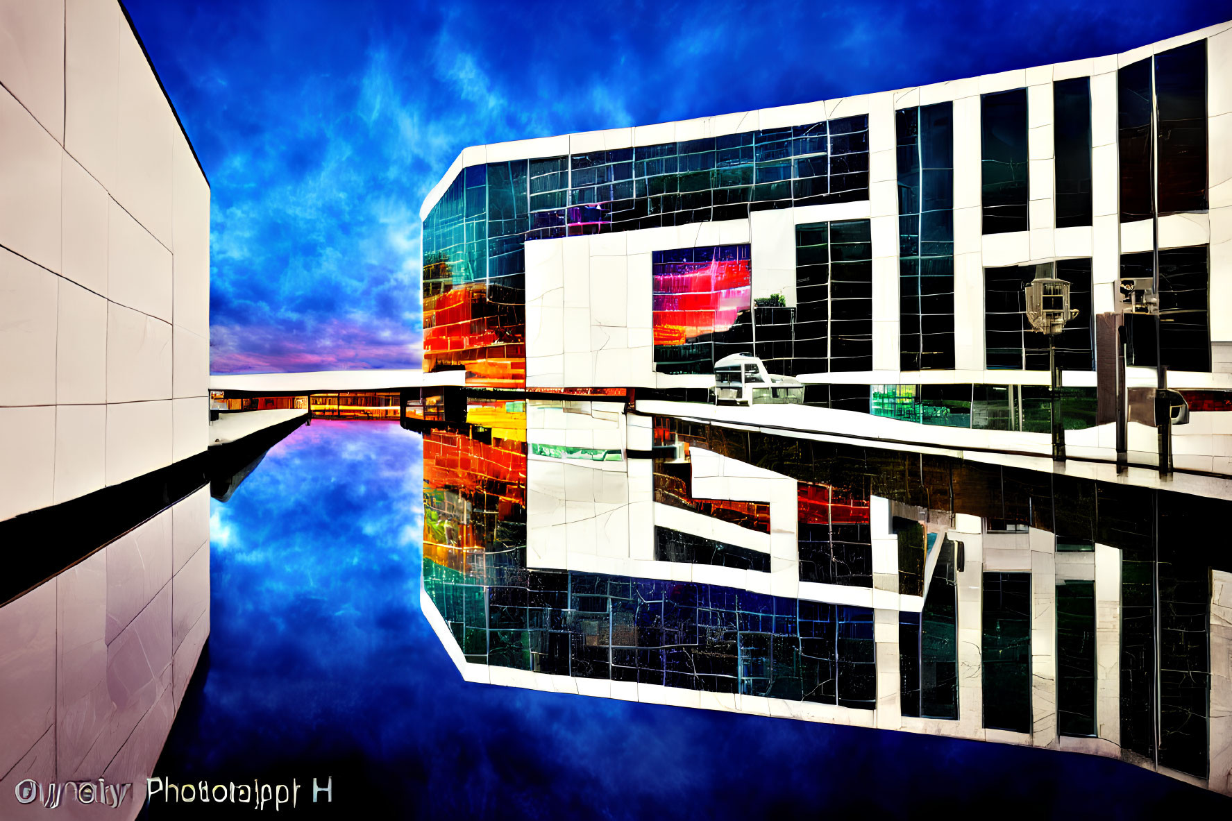 Modern building with reflective glass facade mirrored in water against sunset sky