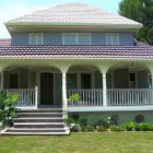 Weathered Two-Story House with Overgrown Vegetation and Dilapidated Porch