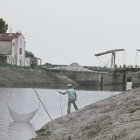 Tranquil riverbank scene with fishing person and sailboat in background