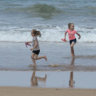 Three girls with colorful parasols on a beach with kites and boats under a cloudy sky