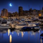 Tranquil harbor night scene with moored boats and city lights reflected under crescent moon