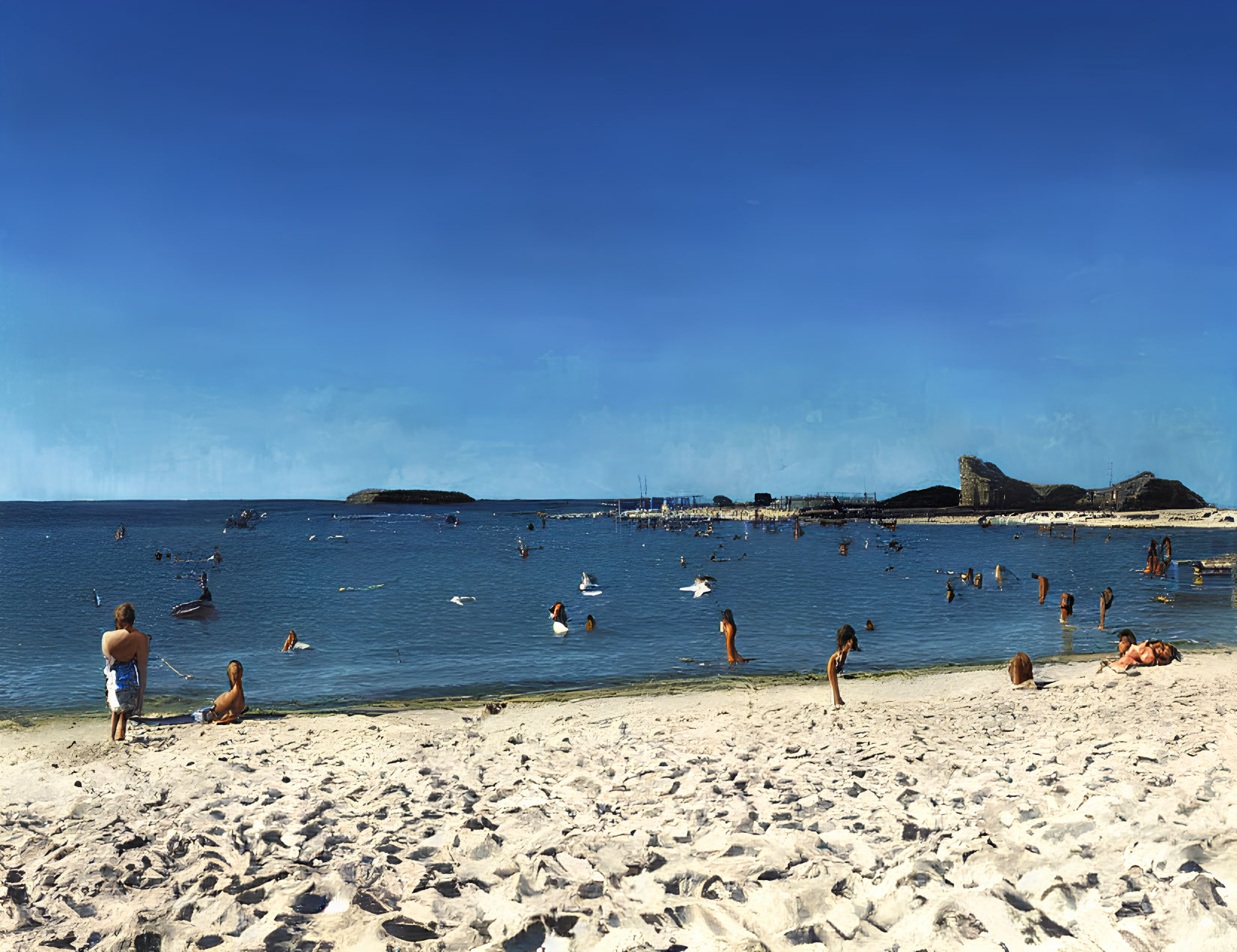 Sunny beach scene with people swimming and lounging on sand