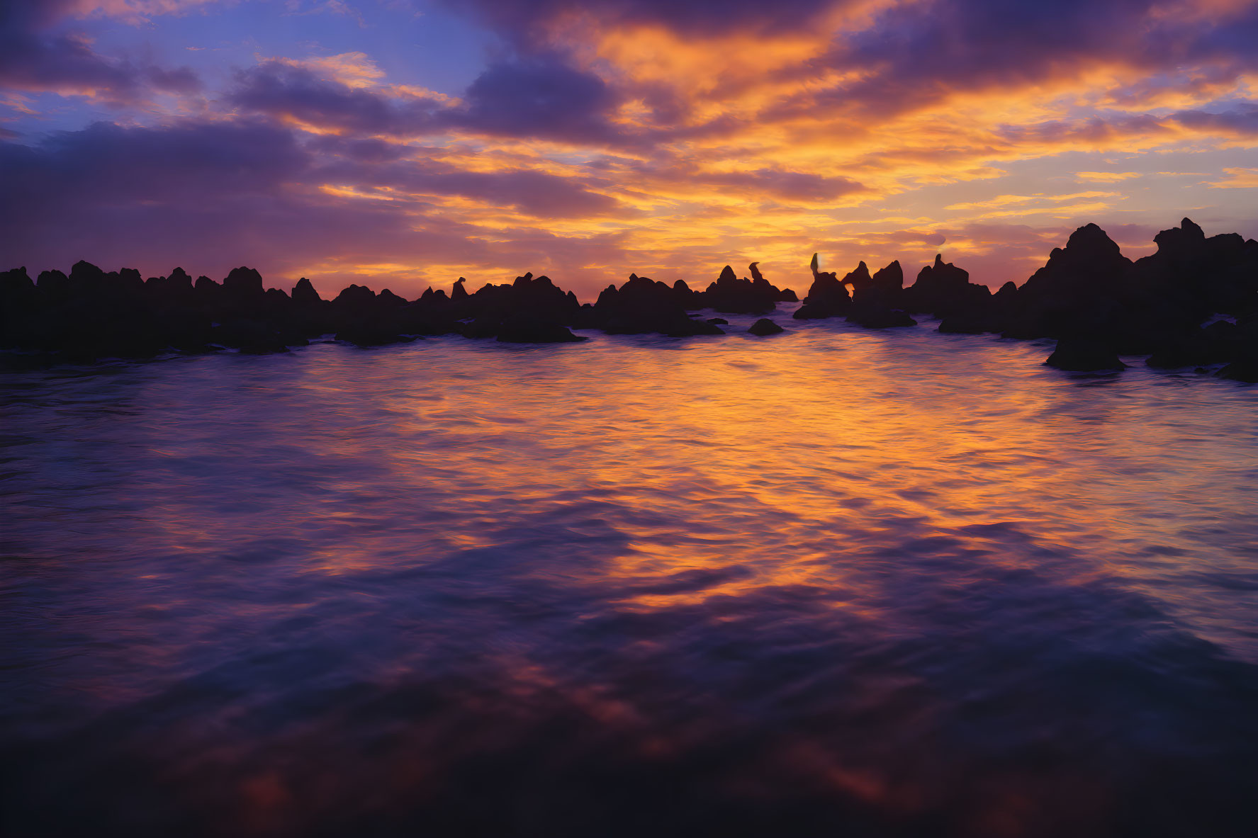 Scenic sunset with cloud reflections on water and silhouetted rocks