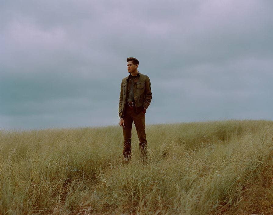 Man standing in tall golden grass under overcast sky in military attire