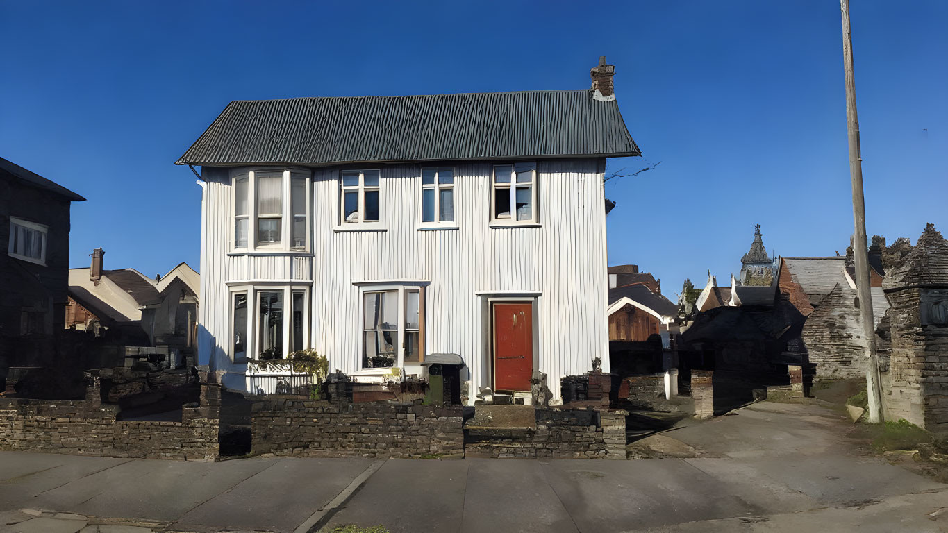 Traditional two-story house with red door, metal roof, stone wall, and blue sky.