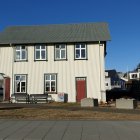 Traditional two-story house with red door, metal roof, stone wall, and blue sky.