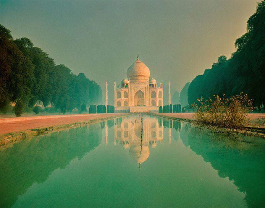 Iconic Taj Mahal reflected in front pool with flanking trees and hazy sky