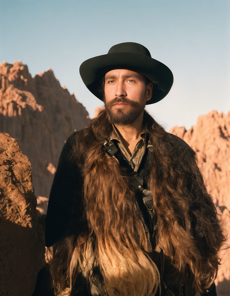 Bearded man in black hat on rocky terrain with fur coat