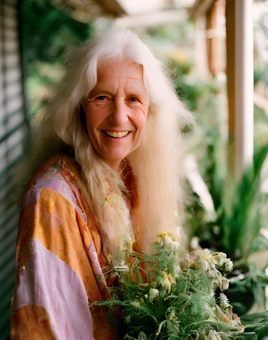 Elderly woman with long white hair holding green plants near window