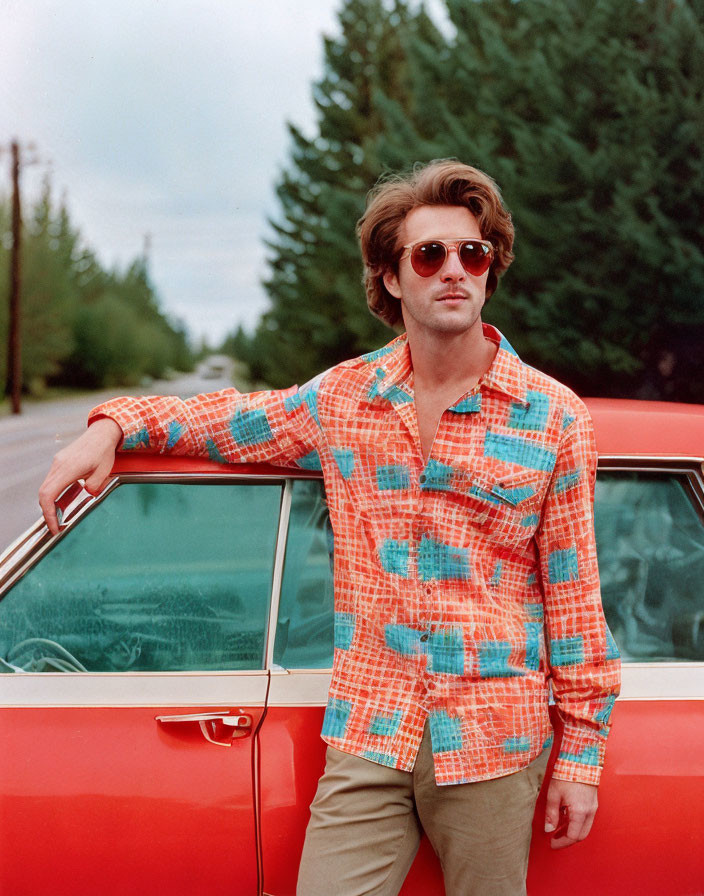 Man in Sunglasses Leaning on Red Car with Colorful Shirt and Trees