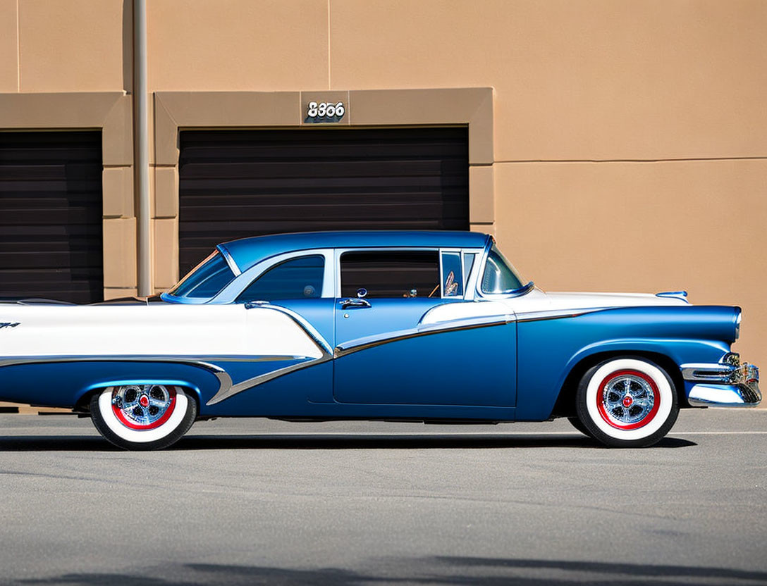 Vintage blue and white car with white-walled tires parked by building with large door number