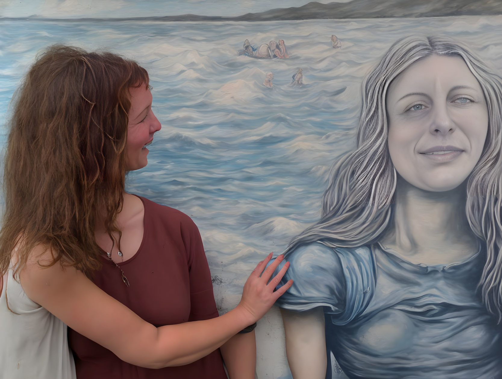 Woman in red dress smiles touching realistic mural of woman amidst ocean swimmers.