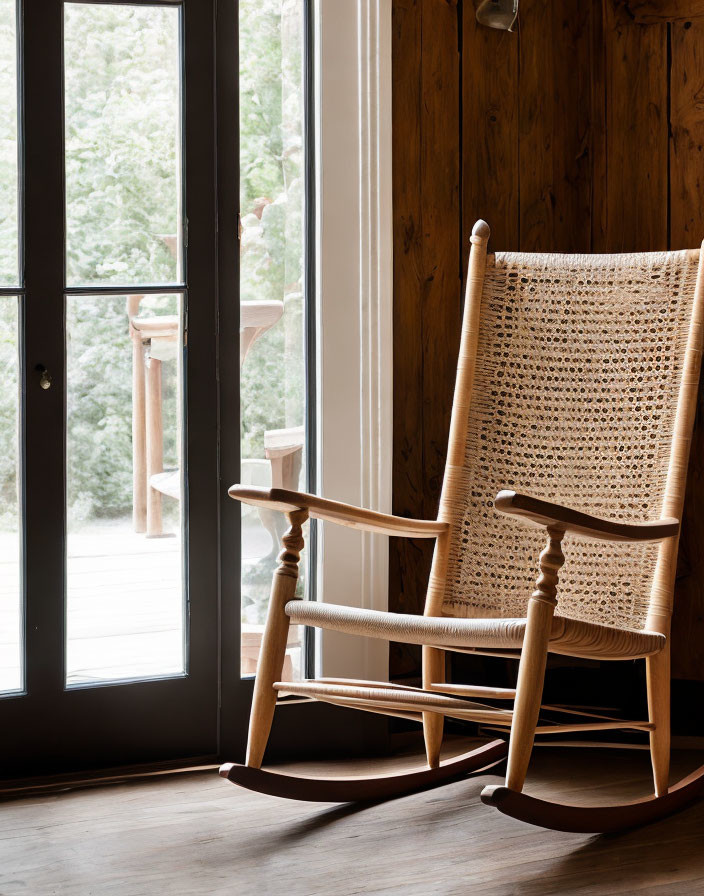 Wooden rocking chair by glass door in cozy rustic room with sunlight and wood paneling