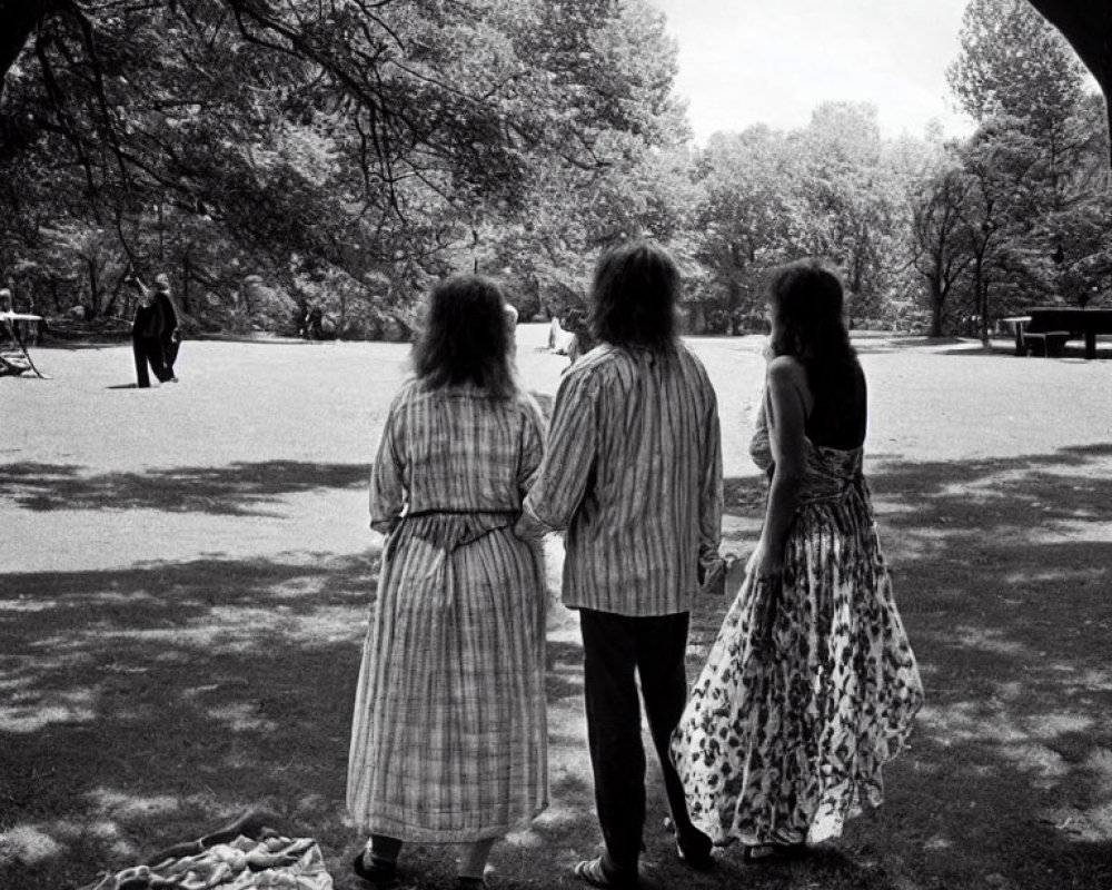 Vintage-dressed trio holding hands in park, gazing at distant figure amid shadowed trees.