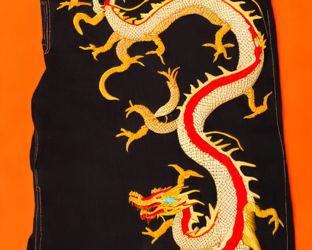 Black jeans with intricate golden dragon embroidery on orange background