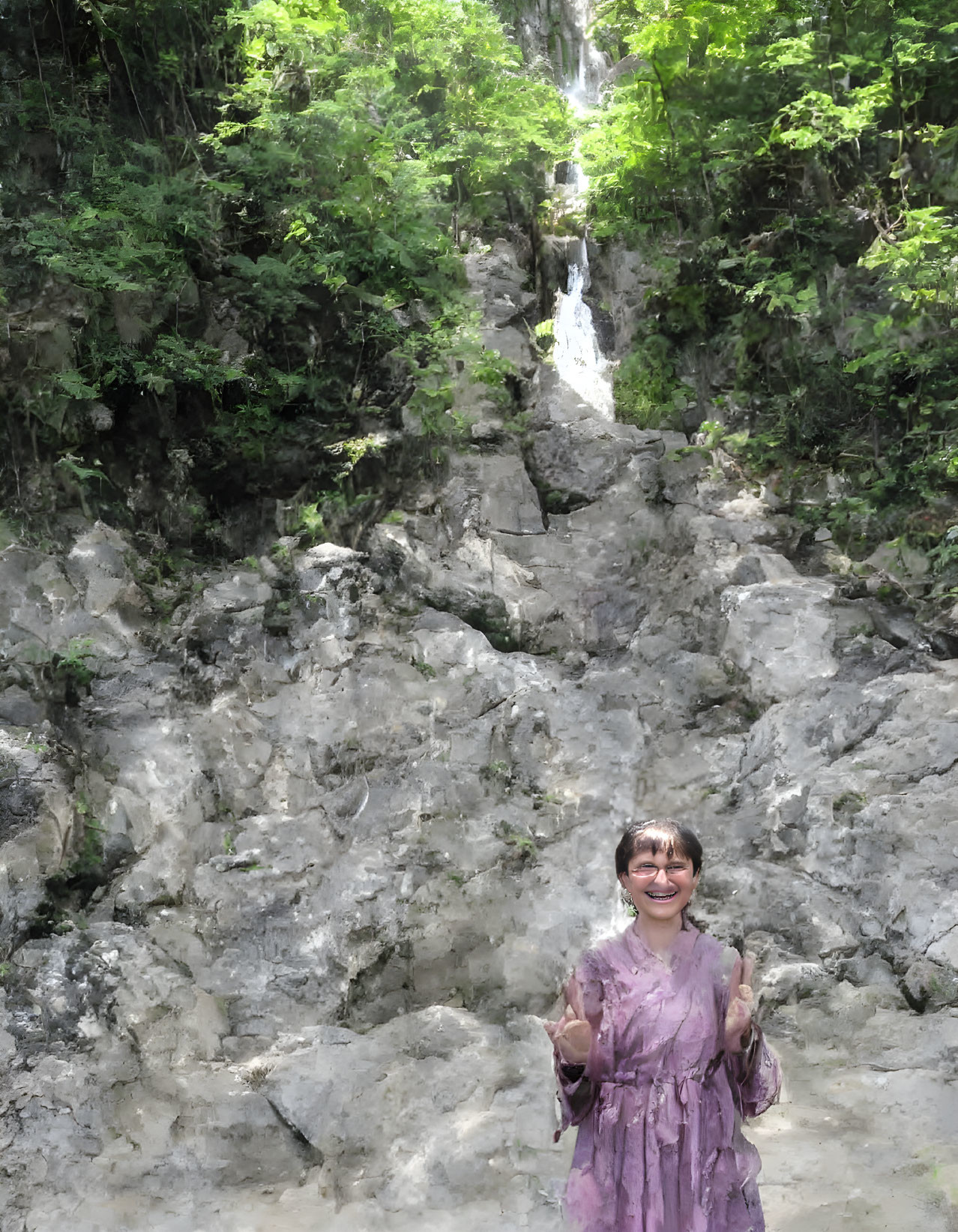 Smiling person in purple dress near small waterfall in lush setting