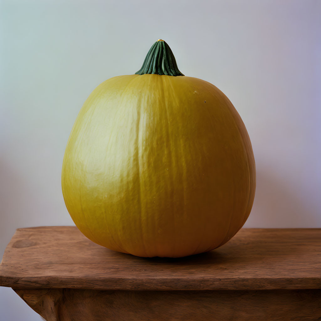 Yellow Pumpkin with Green Stem on Wooden Table against Neutral Background