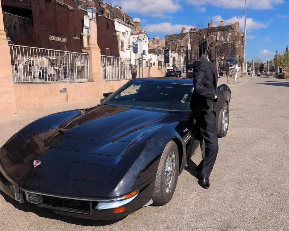 Person in dark clothing leaning on parked black Corvette in sunny street