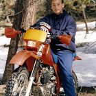 Young boy in oversized clothes with cup by rusty motorcycle on pavement.